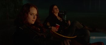Movie still from “We Summon the Darkness” (2019), directed by Marc Meyers – Two women sitting next to each other holding drinks; Medium shot, Over the shoulder angle