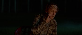 Movie still from “We Summon the Darkness” (2019), directed by Marc Meyers – A man smoking a cigarette while sitting on a bench; Medium shot, Low angle