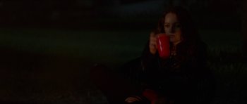 Movie still from “We Summon the Darkness” (2019), directed by Marc Meyers – A woman holding a red cup while sitting on a couch; Medium shot, Over the shoulder angle