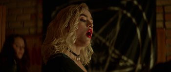 Movie still from “We Summon the Darkness” (2019), directed by Marc Meyers – A woman with blonde curly hair wearing a black top and red lipstick; Close Up shot, Low angle