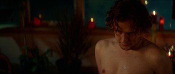 Movie still from “We Summon the Darkness” (2019), directed by Marc Meyers – A man sitting in front of a window with a candle in the background; Close Up shot, High angle