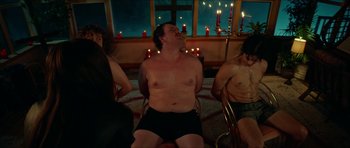 Movie still from “We Summon the Darkness” (2019), directed by Marc Meyers – A man sitting in a chair with two other people in front of a window; Medium shot, High angle