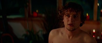 Movie still from “We Summon the Darkness” (2019), directed by Marc Meyers – A man with curly brown hair sitting in a room; Close Up shot, Over the shoulder angle