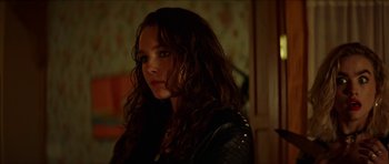 Movie still from “We Summon the Darkness” (2019), directed by Marc Meyers – A woman with long brown curly hair wearing a leather jacket; Close Up shot, Over the shoulder angle