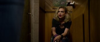 Movie still from “We Summon the Darkness” (2019), directed by Marc Meyers – A woman sitting on a chair in front of a wooden wall; Medium shot, Over the shoulder angle