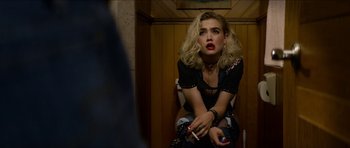 Movie still from “We Summon the Darkness” (2019), directed by Marc Meyers – A woman sitting on a toilet holding a cigarette in her hand; Medium shot, Over the shoulder angle