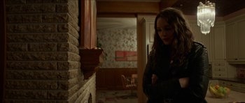 Movie still from “We Summon the Darkness” (2019), directed by Marc Meyers – A woman standing next to a fireplace in a living room; Medium shot, Over the shoulder angle