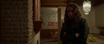 Movie still from “We Summon the Darkness” (2019), directed by Marc Meyers – A woman standing next to a fireplace in a living room; Medium shot, Over the shoulder angle