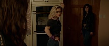 Movie still from “We Summon the Darkness” (2019), directed by Marc Meyers – A woman standing in front of an oven in a kitchen; Medium shot, Over the shoulder angle