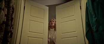 Movie still from “We Summon the Darkness” (2019), directed by Marc Meyers – A woman standing in front of two doors looking at the camera; Medium shot, Low angle