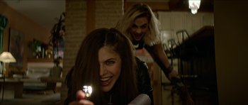 Movie still from “We Summon the Darkness” (2019), directed by Marc Meyers – Two women in a room one is holding a cell phone and the other is holding a cell phone; Medium shot, Over the shoulder angle