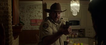 Movie still from “We Summon the Darkness” (2019), directed by Marc Meyers – A man holding a gun while wearing a cowboy hat; Medium shot, Over the shoulder angle