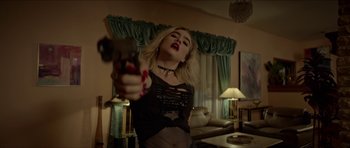 Movie still from “We Summon the Darkness” (2019), directed by Marc Meyers – A woman holding a gun in a living room; Medium shot, Over the shoulder angle