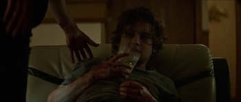 Movie still from “We Summon the Darkness” (2019), directed by Marc Meyers – A man drinking a glass of water with blood on his face; Medium shot, Over the shoulder angle