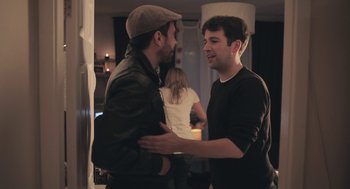 Movie still from “Weekend” (2011), directed by Andrew Haigh – Two young men embracing each other in front of a group of people; Medium shot, Over the shoulder angle