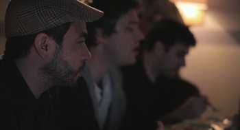 Movie still from “Weekend” (2011), directed by Andrew Haigh – A group of men sitting next to each other in a dark room; Close Up shot, Over the shoulder angle
