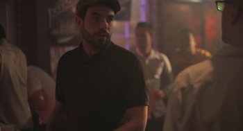 Movie still from “Weekend” (2011), directed by Andrew Haigh – A bearded man wearing a hat standing next to another man; Medium shot, Over the shoulder angle