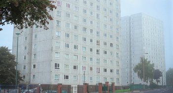 Movie still from “Weekend” (2011), directed by Andrew Haigh – A tall white building with many windows on the outside; Extreme Wide shot, Low angle