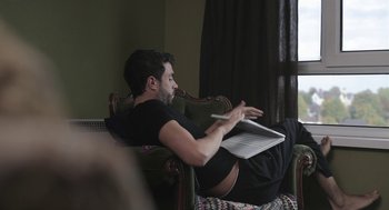 Movie still from “Weekend” (2011), directed by Andrew Haigh – A man sitting in a chair holding a laptop; Medium shot, Low angle