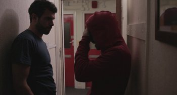 Movie still from “Weekend” (2011), directed by Andrew Haigh – A man in a red hooded jacket is looking at another man; Medium shot, Over the shoulder angle