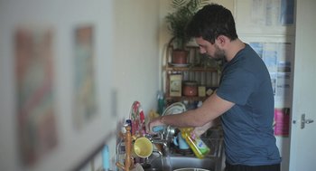 Movie still from “Weekend” (2011), directed by Andrew Haigh – A man is washing dishes in the kitchen sink; Medium shot, Low angle