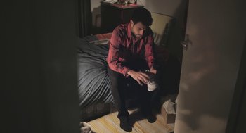 Movie still from “Weekend” (2011), directed by Andrew Haigh – A man sitting on the floor in a room; Medium shot, Low angle