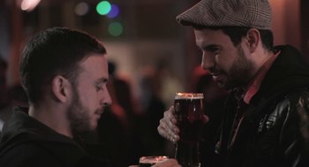 Movie still from “Weekend” (2011), directed by Andrew Haigh – Two men sitting at a table with a glass of beer; Close Up shot, Over the shoulder angle