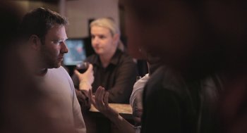 Movie still from “Weekend” (2011), directed by Andrew Haigh – A group of people sitting at a table talking to each other; Medium shot, Over the shoulder angle
