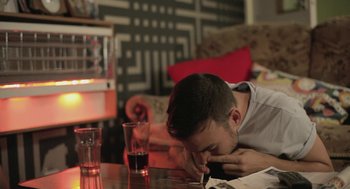 Movie still from “Weekend” (2011), directed by Andrew Haigh – A young man sitting at a table with a glass of wine; Medium shot, Low angle