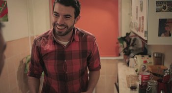 Movie still from “Weekend” (2011), directed by Andrew Haigh – A man in a red and black shirt smiling; Medium shot, Over the shoulder angle