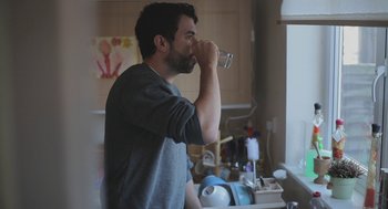 Movie still from “Weekend” (2011), directed by Andrew Haigh – A man drinking a glass of water in a room; Medium shot, Over the shoulder angle
