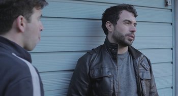 Movie still from “Weekend” (2011), directed by Andrew Haigh – A man wearing a leather jacket standing next to another man; Close Up shot, Over the shoulder angle