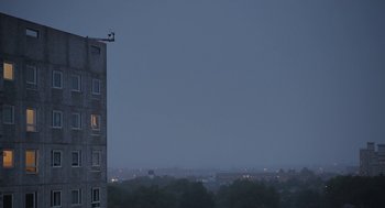 Movie still from “Weekend” (2011), directed by Andrew Haigh – A bird sitting on top of a building near a window; Extreme Wide shot, Low angle