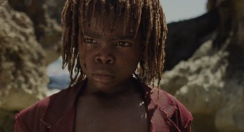 A child with dreadlocks is standing in the dirt