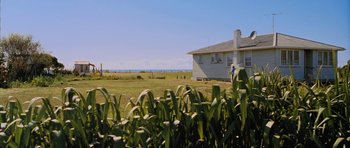Movie still from “Whale Rider” (2002), directed by Niki Caro – A white house sitting on top of a grass covered field; Extreme Wide shot, Low angle