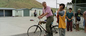 Movie still from “Whale Rider” (2002), directed by Niki Caro – An older man riding a bike on a paved road; Wide shot, Over the shoulder angle