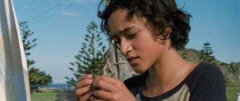 Movie still from “Whale Rider” (2002), directed by Niki Caro – A young boy looking down while holding a string in his hands; Close Up shot, Low angle