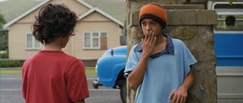 Movie still from “Whale Rider” (2002), directed by Niki Caro – A young man smoking a cigarette while standing next to a building; Medium shot, Over the shoulder angle