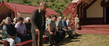Movie still from “Whale Rider” (2002), directed by Niki Caro – A group of men sitting on a bench in front of a building; Wide shot, Over the shoulder angle