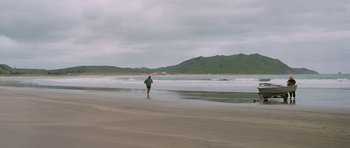 Movie still from “Whale Rider” (2002), directed by Niki Caro – A man walking on the beach with a surfboard; Extreme Wide shot, High angle