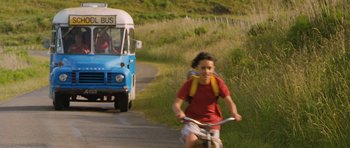 Movie still from “Whale Rider” (2002), directed by Niki Caro – A boy riding a bike down a road next to a bus; Wide shot, Low angle