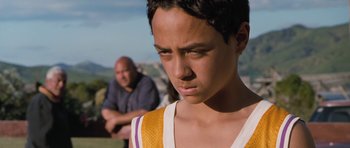 Movie still from “Whale Rider” (2002), directed by Niki Caro – A young boy is looking at the camera while a man sits in the background; Close Up shot, Over the shoulder angle