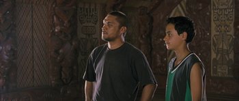 Movie still from “Whale Rider” (2002), directed by Niki Caro – A man standing next to a woman in front of a wooden wall; Medium shot, Over the shoulder angle