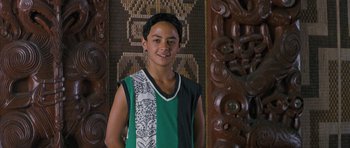 Movie still from “Whale Rider” (2002), directed by Niki Caro – A young man standing in front of a wooden wall; Medium shot, High angle