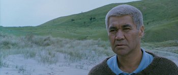 Movie still from “Whale Rider” (2002), directed by Niki Caro – An older man standing in front of a grassy hill; Close Up shot, Over the shoulder angle