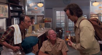 Movie still from “What About Bob?” (1991), directed by Frank Oz – A group of men sitting around a table in front of a bar; Medium shot, Over the shoulder angle
