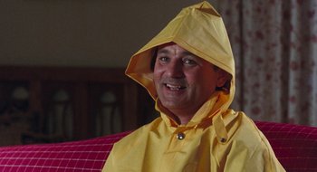 Movie still from “What About Bob?” (1991), directed by Frank Oz – A man in a yellow raincoat is smiling for the camera; Close Up shot, Low angle