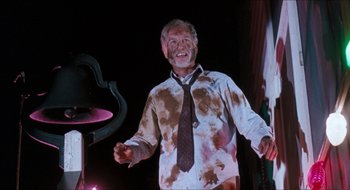 Movie still from “What About Bob?” (1991), directed by Frank Oz – A man in a brown tie standing in front of a microphone; Medium shot, Low angle