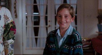 Movie still from “What About Bob?” (1991), directed by Frank Oz – A young boy wearing a sweater smiling for the camera; Medium shot, Low angle