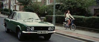 Movie still from “What Have You Done to Solange?” (1972), directed by Massimo Dallamano – A woman riding a bike down a street next to a car; Wide shot, High angle